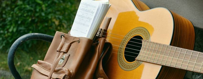 Een gitaar waar een schooltas voor staat met bladmuziek er in