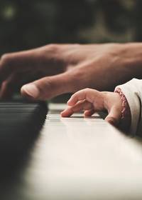 Een hand van een volwassene en een hand van een kind op een klavier