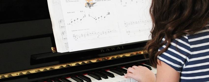 Een meisje dat achter ene piano aan het spelen is met een pianoboek